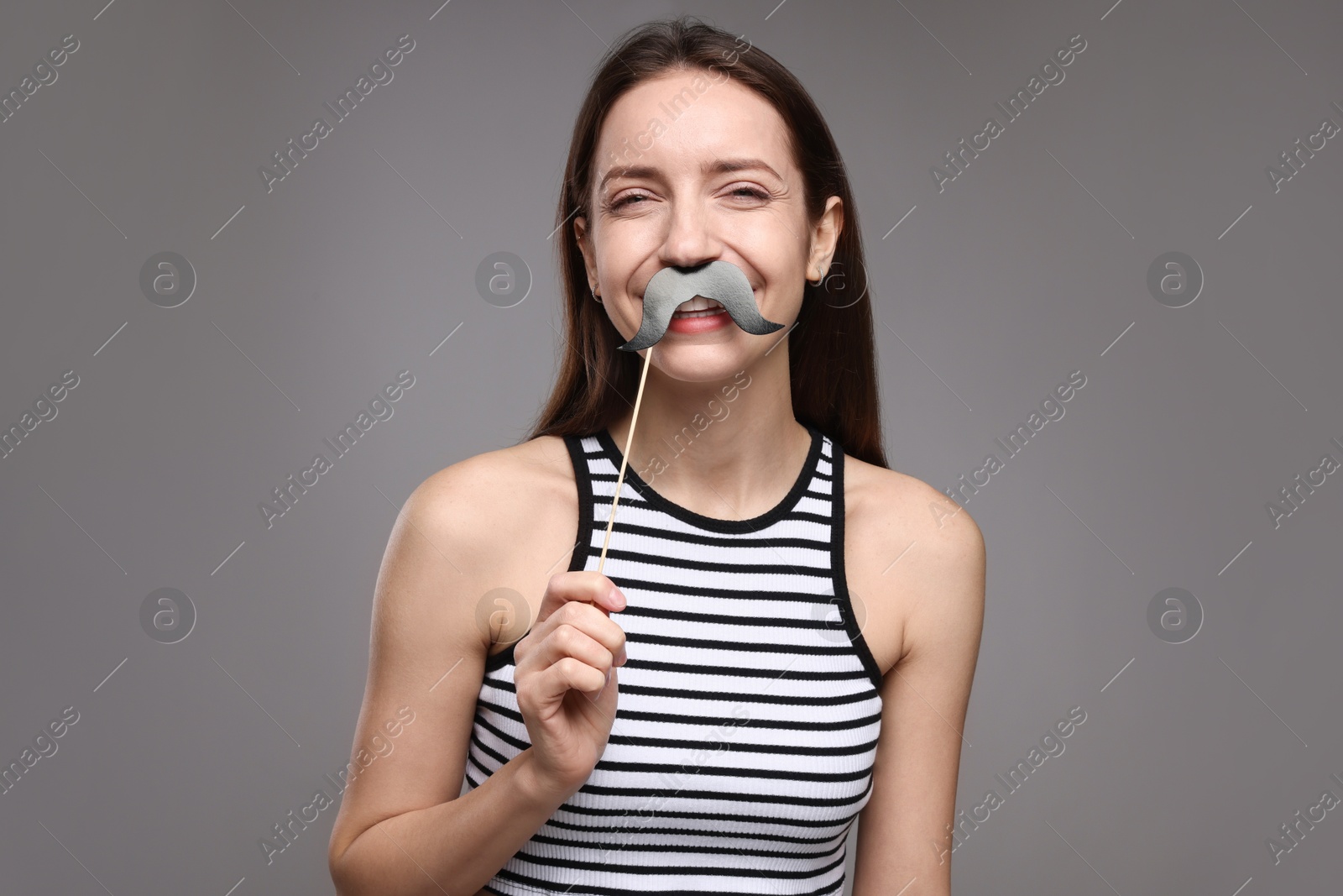 Photo of Smiling woman with fake paper mustache on grey background