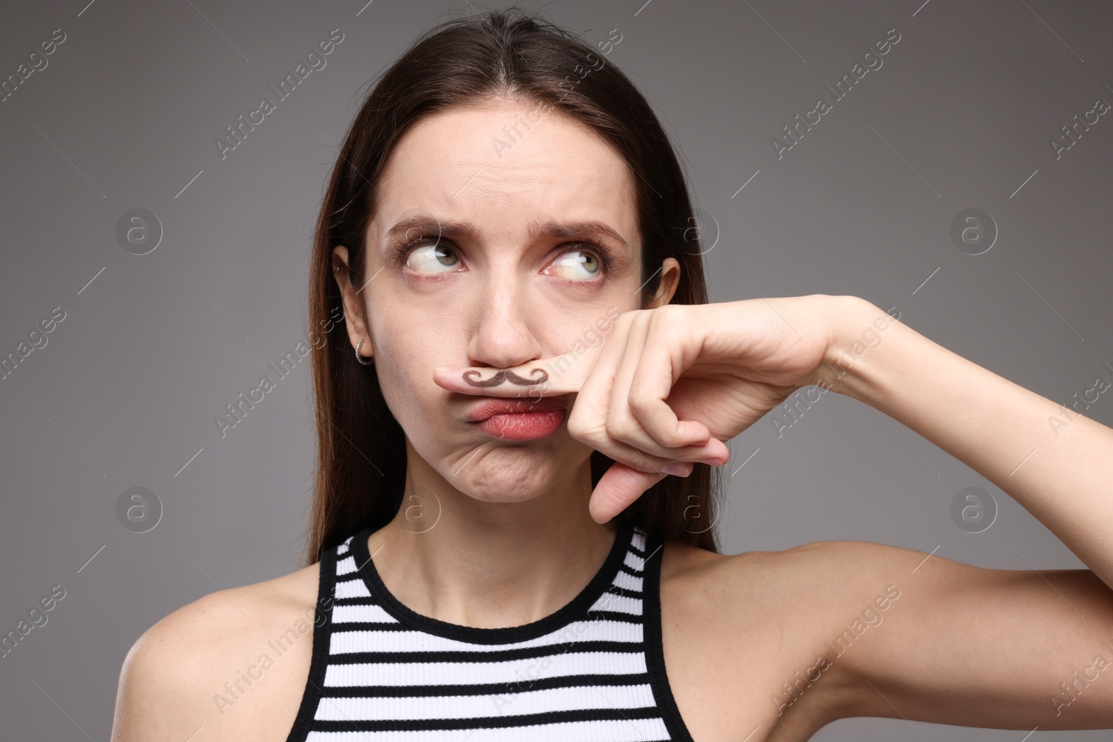 Photo of Funny woman holding finger with drawn mustache above lips on grey background