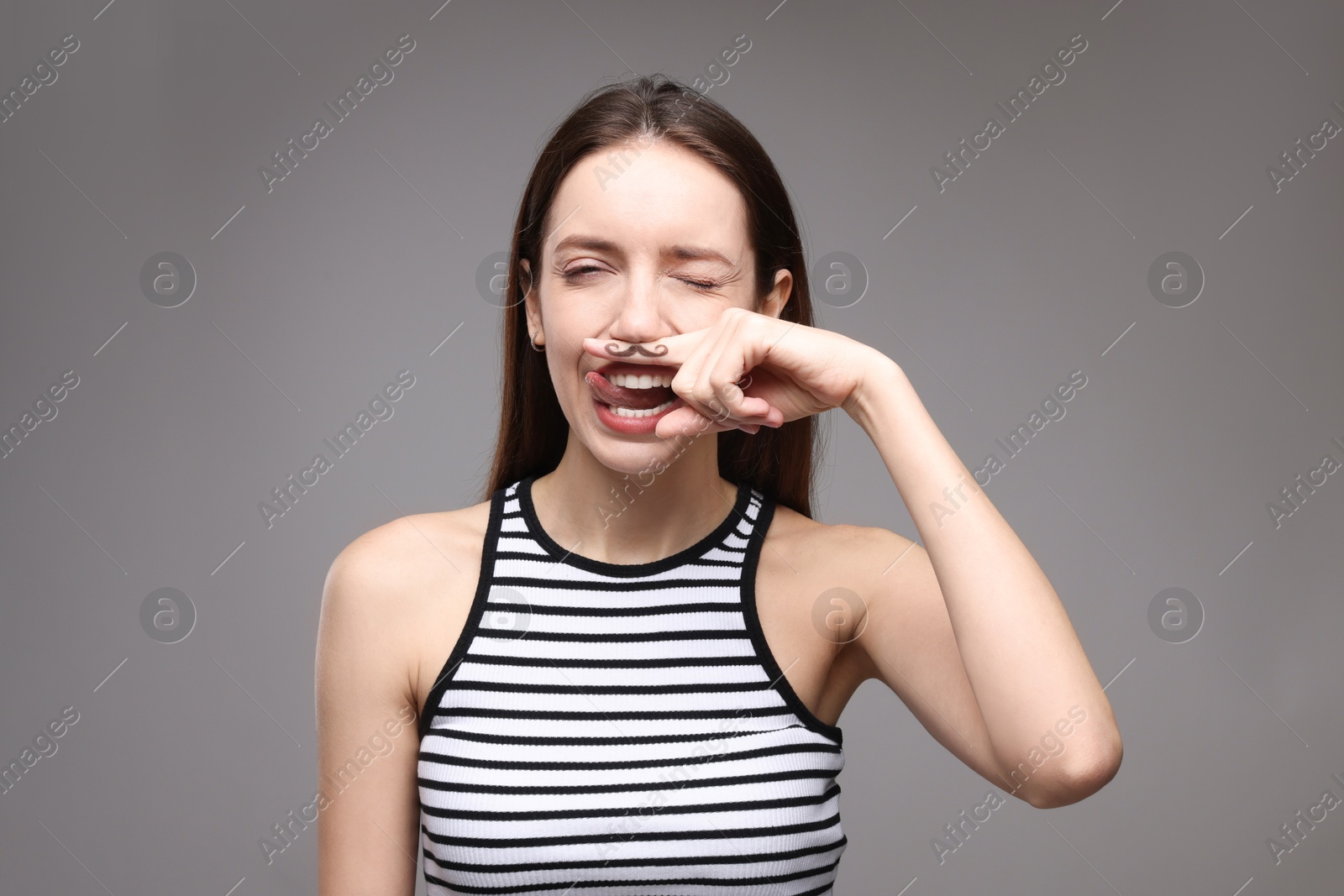 Photo of Funny woman holding finger with drawn mustache above lips on grey background