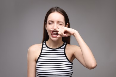 Photo of Funny woman holding finger with drawn mustache above lips on grey background