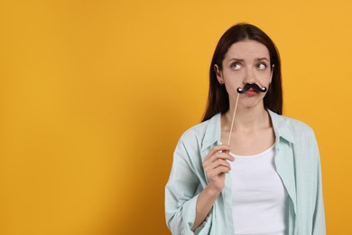 Photo of Thoughtful woman with fake paper mustache on orange background. Space for text