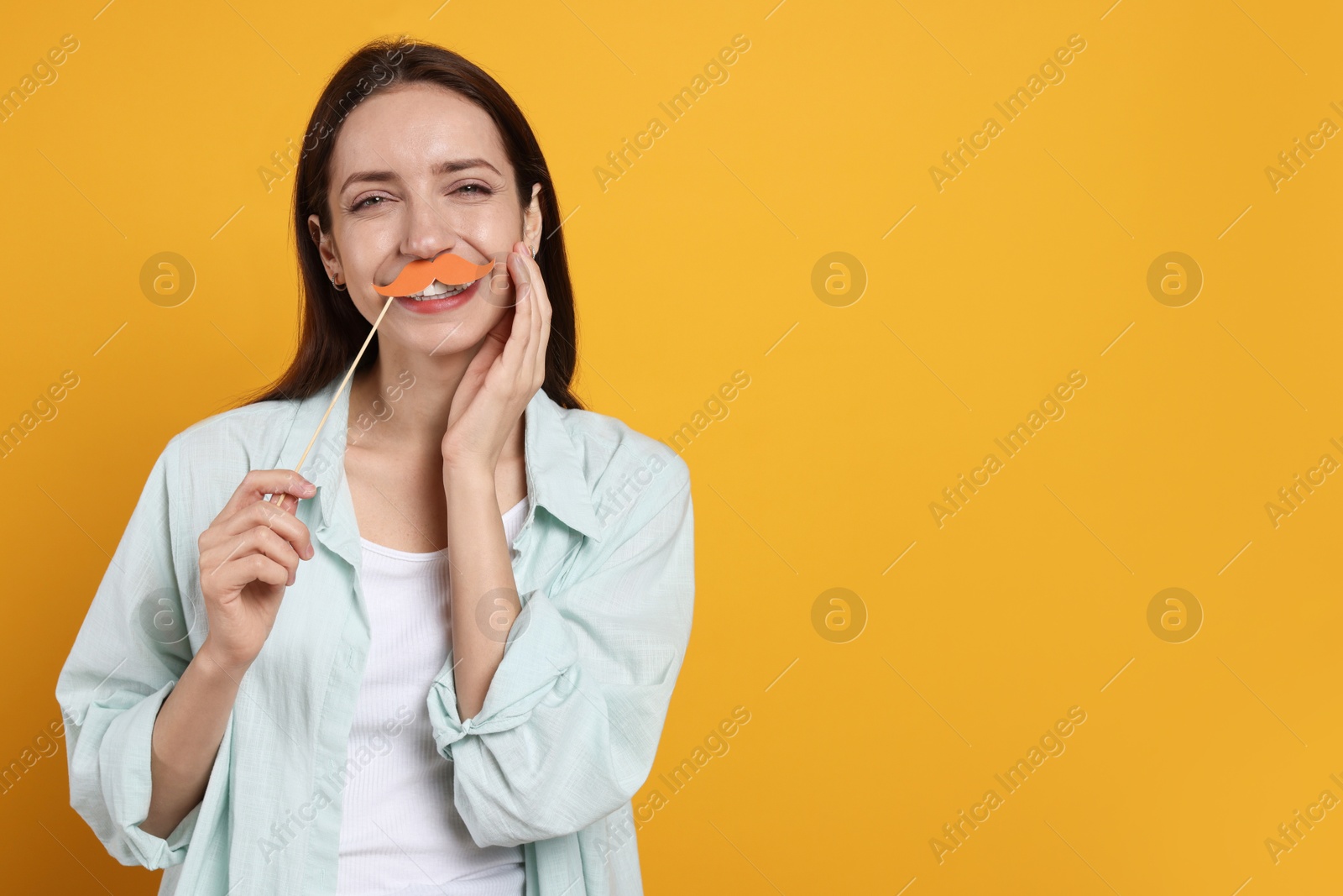 Photo of Happy woman with fake paper mustache on orange background. Space for text