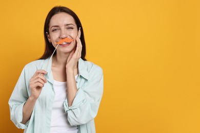 Photo of Happy woman with fake paper mustache on orange background. Space for text