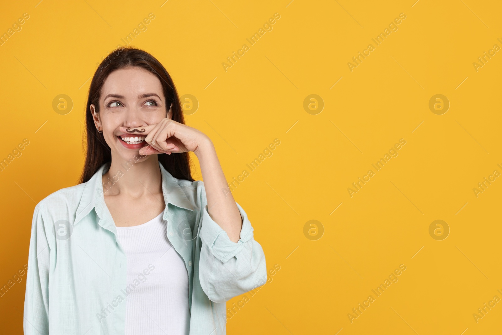 Photo of Happy woman holding finger with drawn mustache above lips on orange background. Space for text