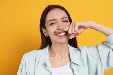 Photo of Happy woman holding finger with drawn mustache above lips on orange background