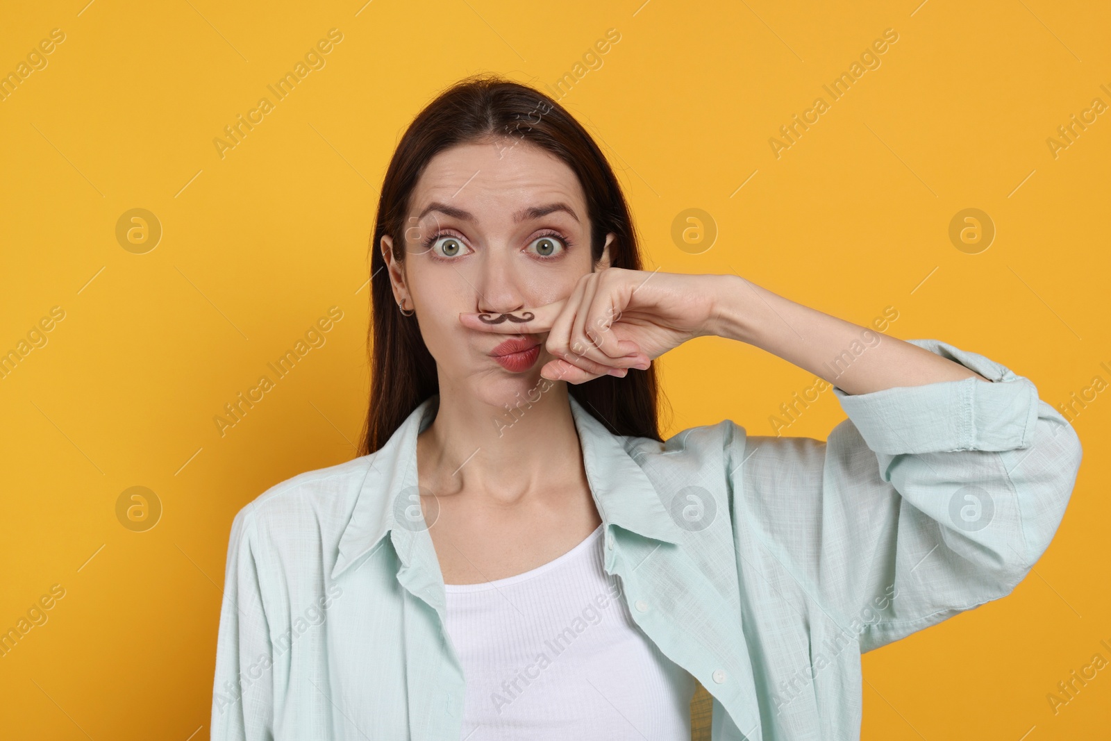 Photo of Funny woman holding finger with drawn mustache above lips on orange background