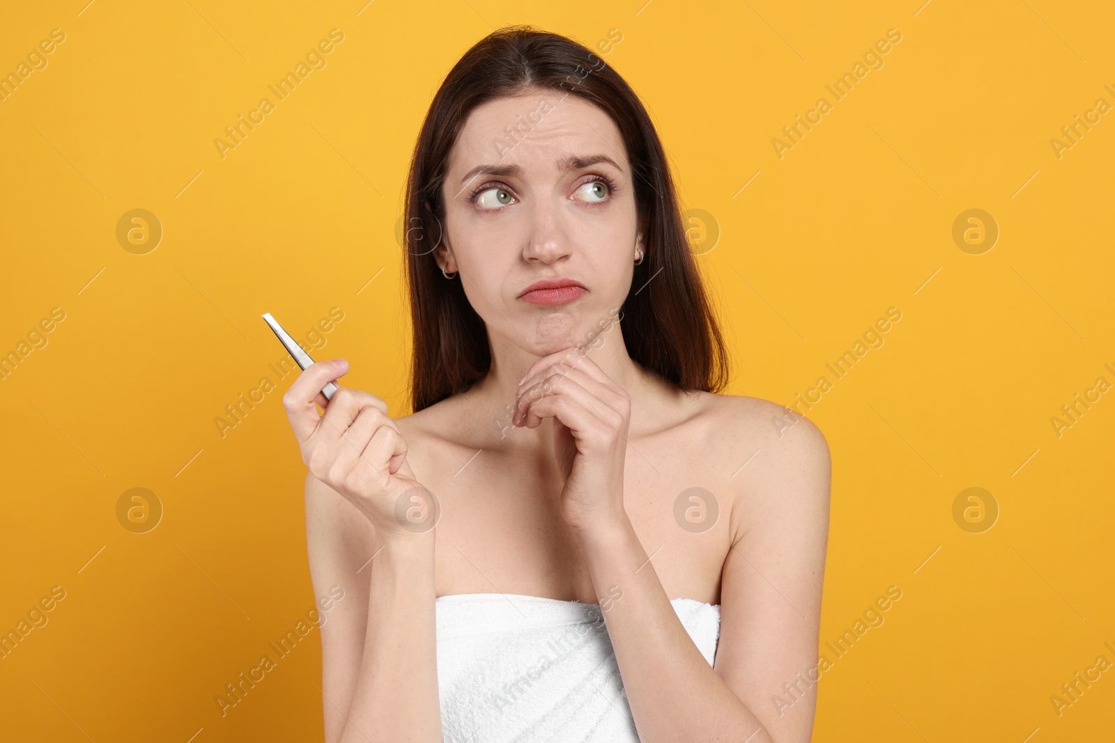 Photo of Thoughtful woman with tweezers on orange background. Mustache removal tool