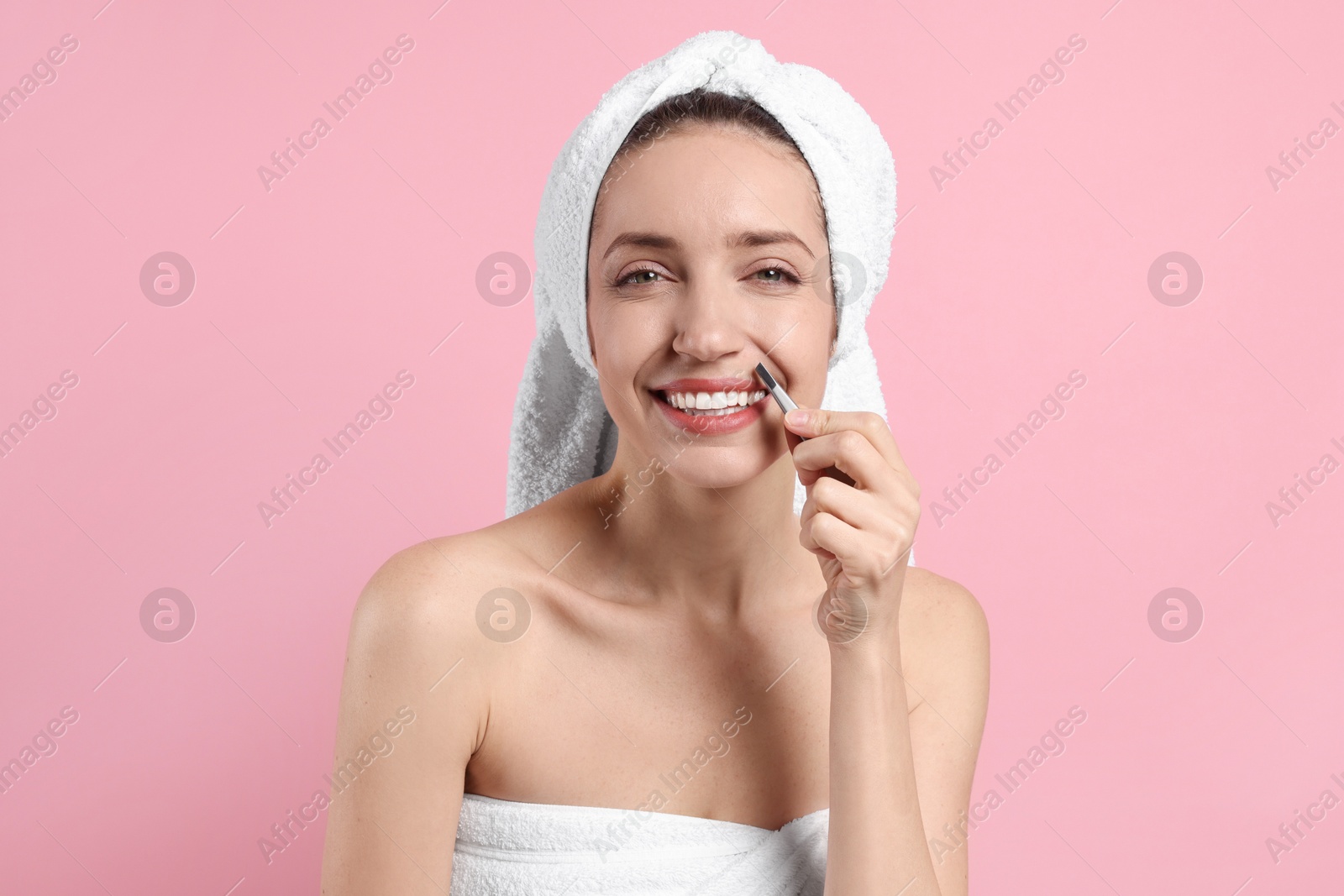 Photo of Happy woman plucking her mustache with tweezers on pink background