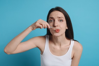 Photo of Woman plucking her mustache with tweezers on light blue background