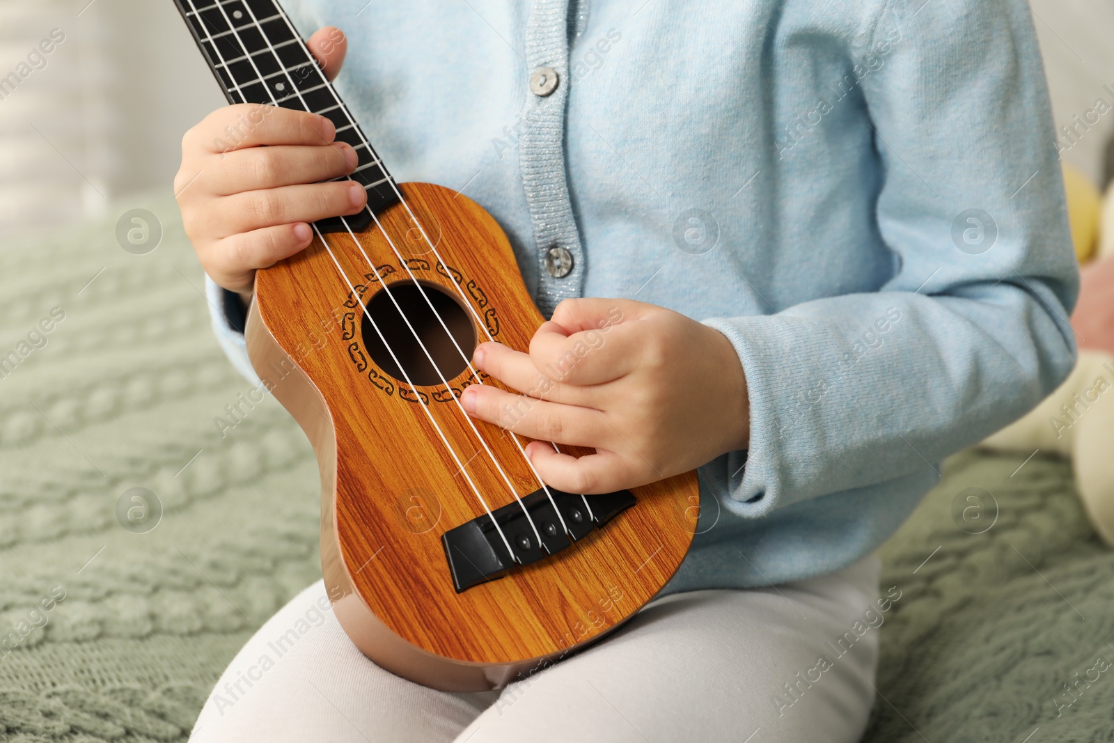 Photo of Little girl with ukulele on bed at home, closeup