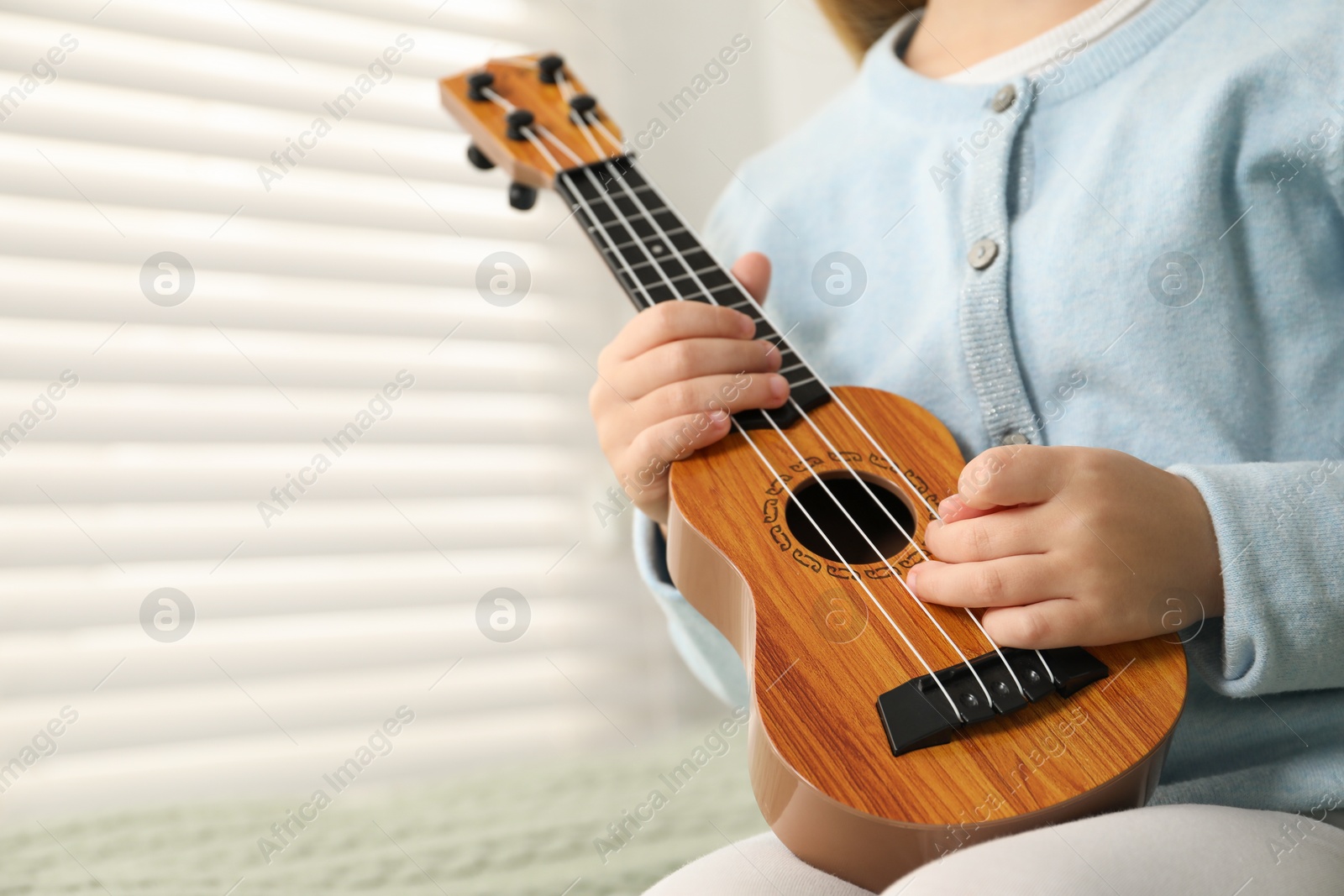 Photo of Little girl with ukulele on bed at home, closeup. Space for text