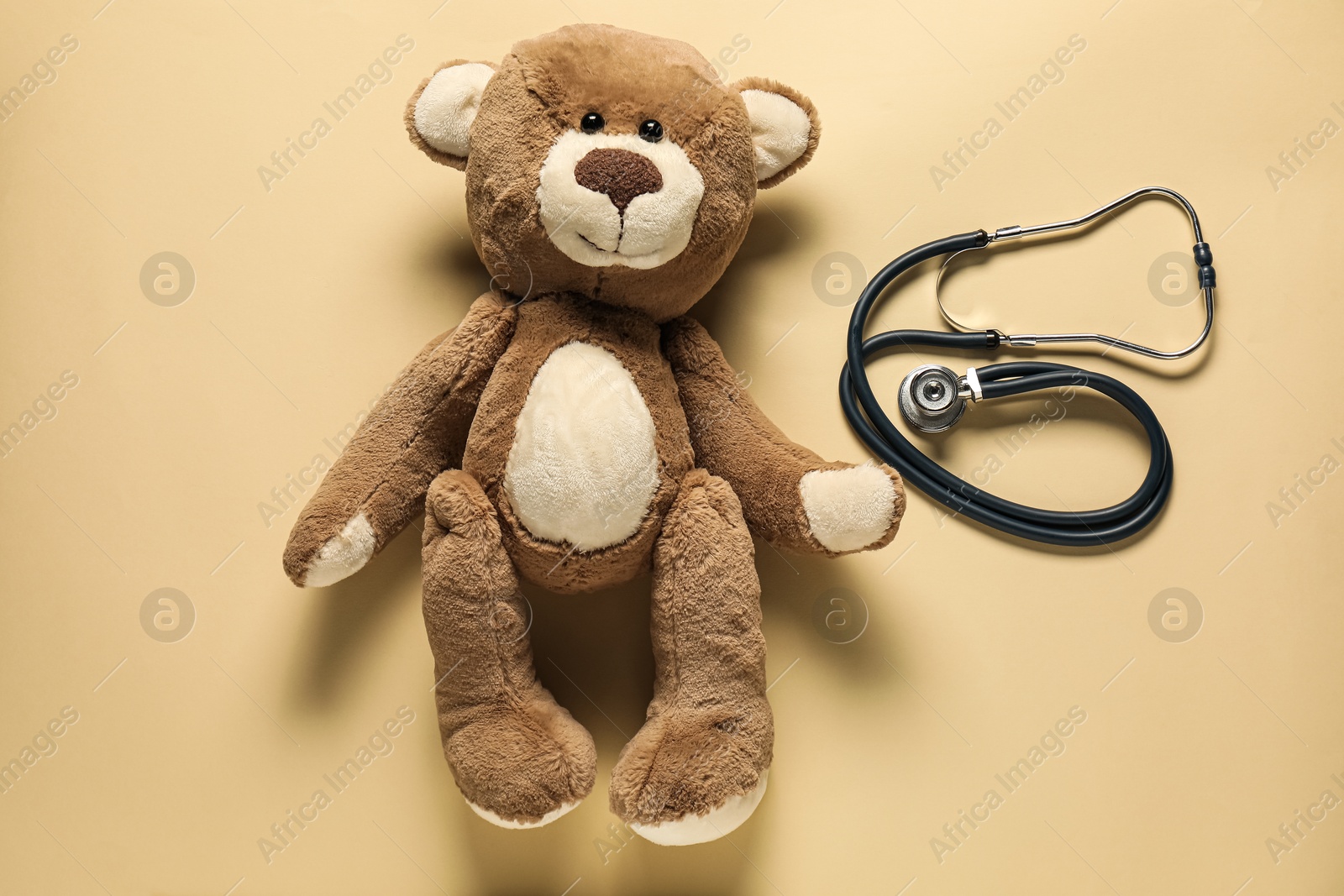 Photo of Pediatrics concept. Teddy bear with stethoscope on beige background, top view