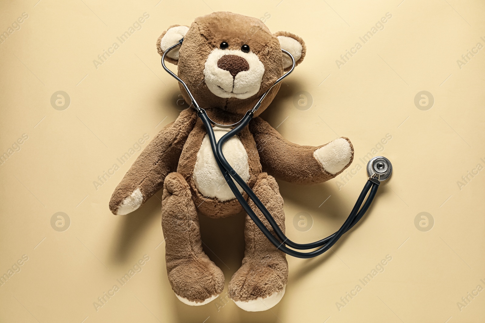 Photo of Pediatrics concept. Teddy bear with stethoscope on beige background, top view