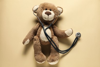 Photo of Pediatrics concept. Teddy bear with stethoscope on beige background, top view