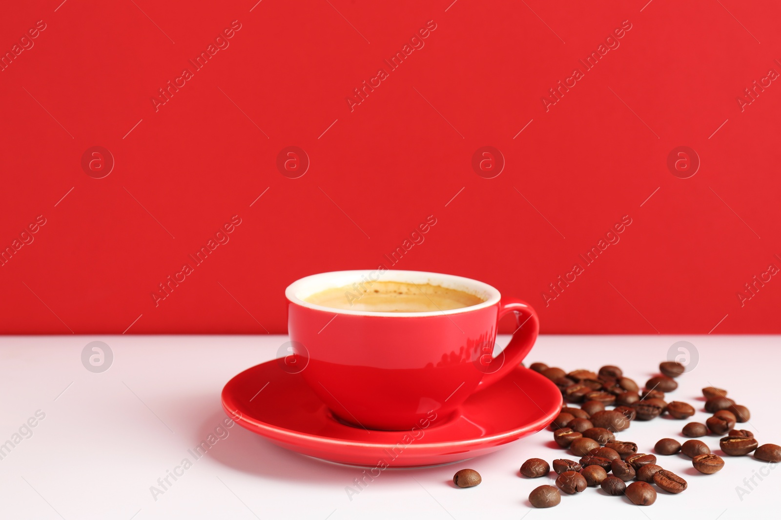 Red cup with coffee and roasted beans on white table, space for text Photo of Red cup with coffee and roasted beans on white table, space for text