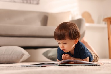 Photo of Cute little boy with book on floor at home, space for text