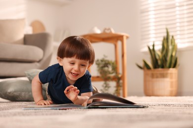 Photo of Cute little boy with book on floor at home