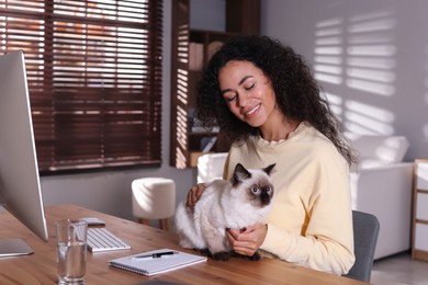 Photo of Beautiful woman with her cute cat working on computer at desk in home office