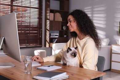 Beautiful woman with her cute cat working on computer at desk in home office