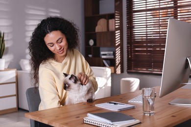 Photo of Beautiful woman with her cute cat working on computer at desk in home office