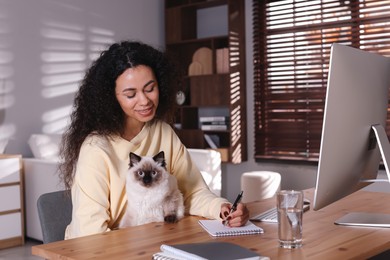 Photo of Beautiful woman with her cute cat working on computer at desk in home office