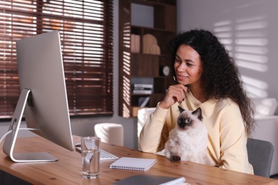 Photo of Beautiful woman with her cute cat working on computer at desk in home office