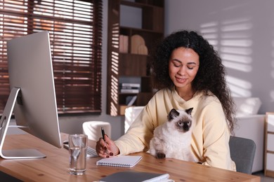 Photo of Beautiful woman with her cute cat working on computer at desk in home office