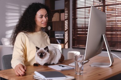 Photo of Beautiful woman with her cute cat working on computer at desk in home office