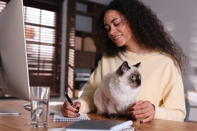 Photo of Beautiful woman with her cute cat working on computer at desk in home office