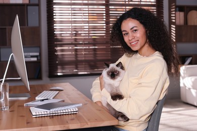 Photo of Beautiful woman with her cute cat working on computer at desk in home office