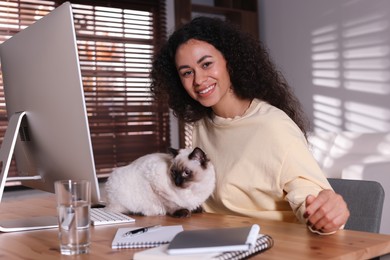 Photo of Beautiful woman with her cute cat working on computer at desk in home office