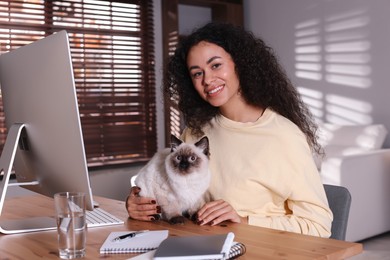 Photo of Beautiful woman with her cute cat working on computer at desk in home office