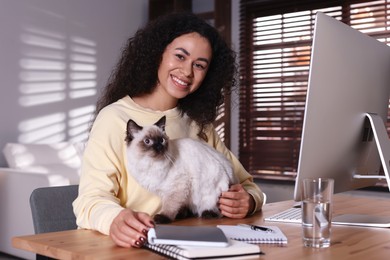 Photo of Beautiful woman with her cute cat working on computer at desk in home office