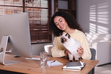 Photo of Beautiful woman with her cute cat working on computer at desk in home office