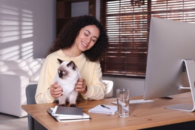 Photo of Beautiful woman with her cute cat working on computer at desk in home office