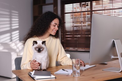 Photo of Beautiful woman with her cute cat working on computer at desk in home office