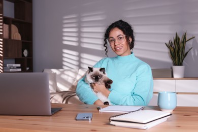 Photo of Beautiful woman with her cute cat working on laptop at desk in home office