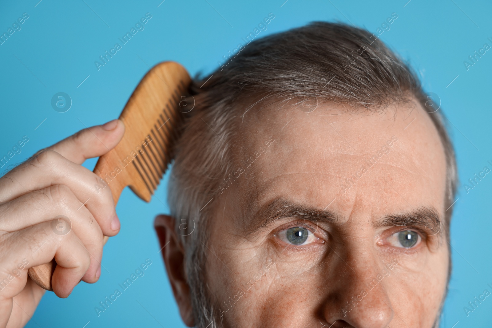 Photo of Man combing his hair on light blue background, closeup