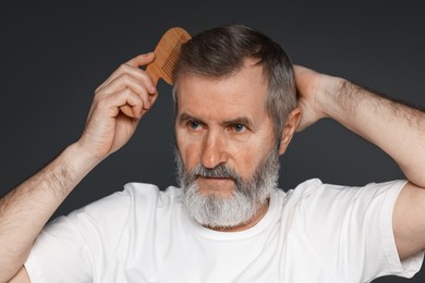 Photo of Handsome man combing his hair on dark grey background