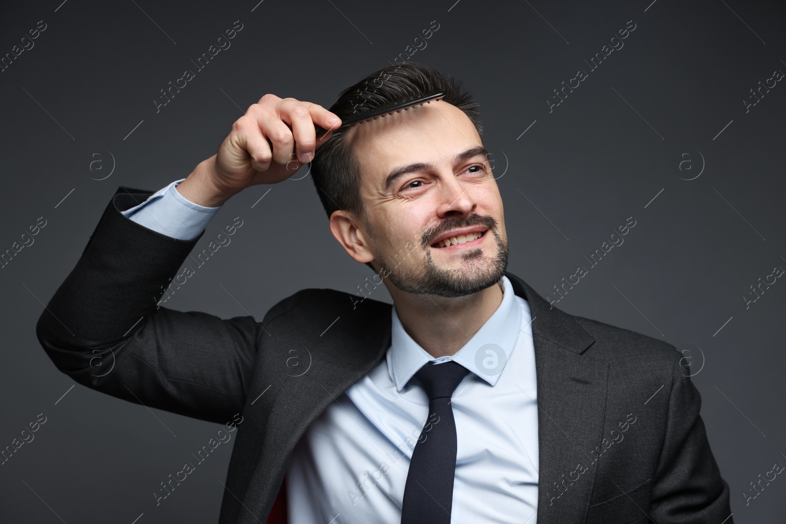 Photo of Handsome businessman combing his hair on dark background