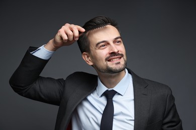 Handsome businessman combing his hair on dark background