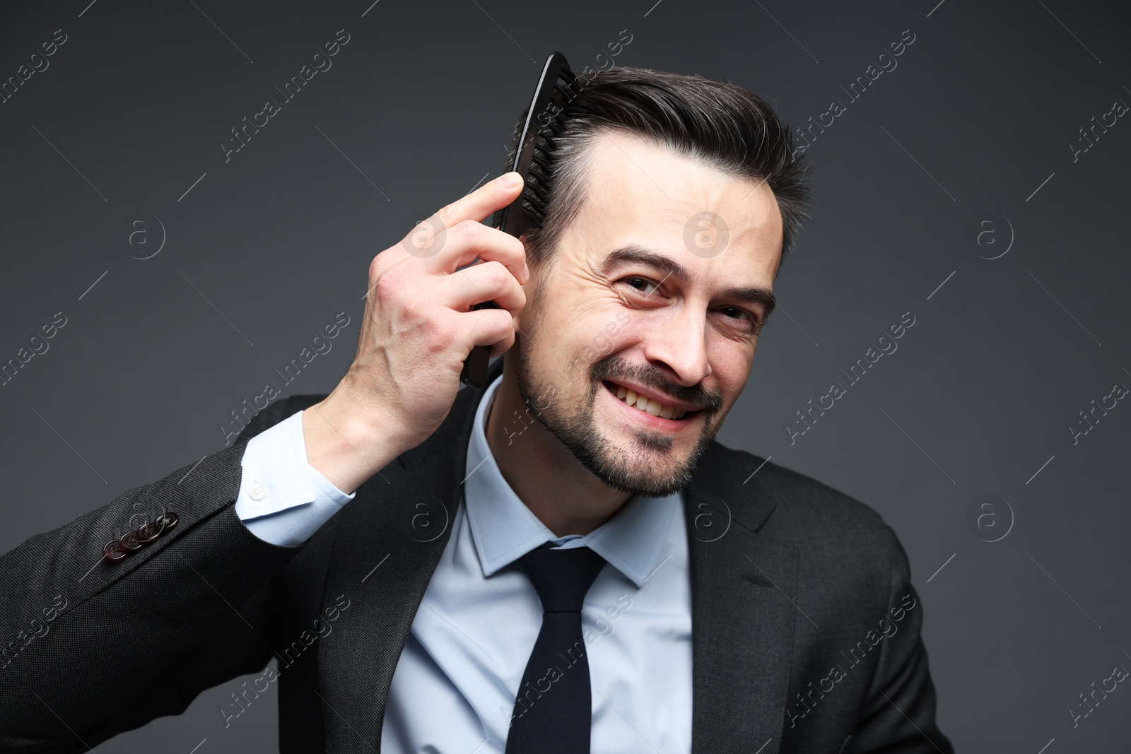 Photo of Handsome businessman combing his hair on dark background