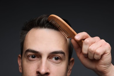 Photo of Handsome man combing his hair on dark background, closeup