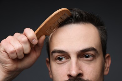 Photo of Handsome man combing his hair on dark background, closeup