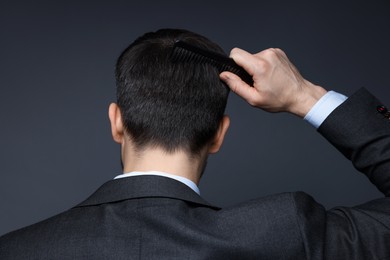 Photo of Man combing his hair on dark background, back view