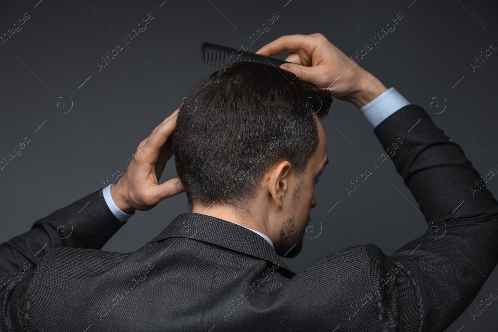 Photo of Man combing his hair on dark background, back view