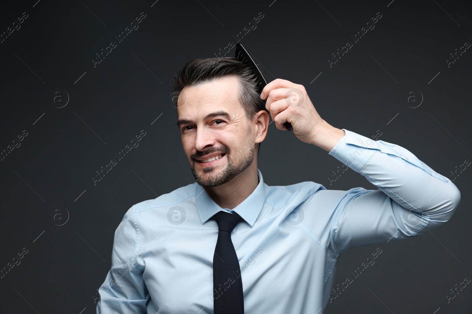 Photo of Handsome man combing his hair on dark background