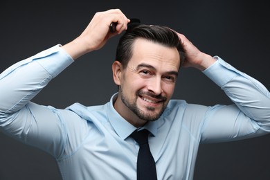 Photo of Handsome man combing his hair on dark background