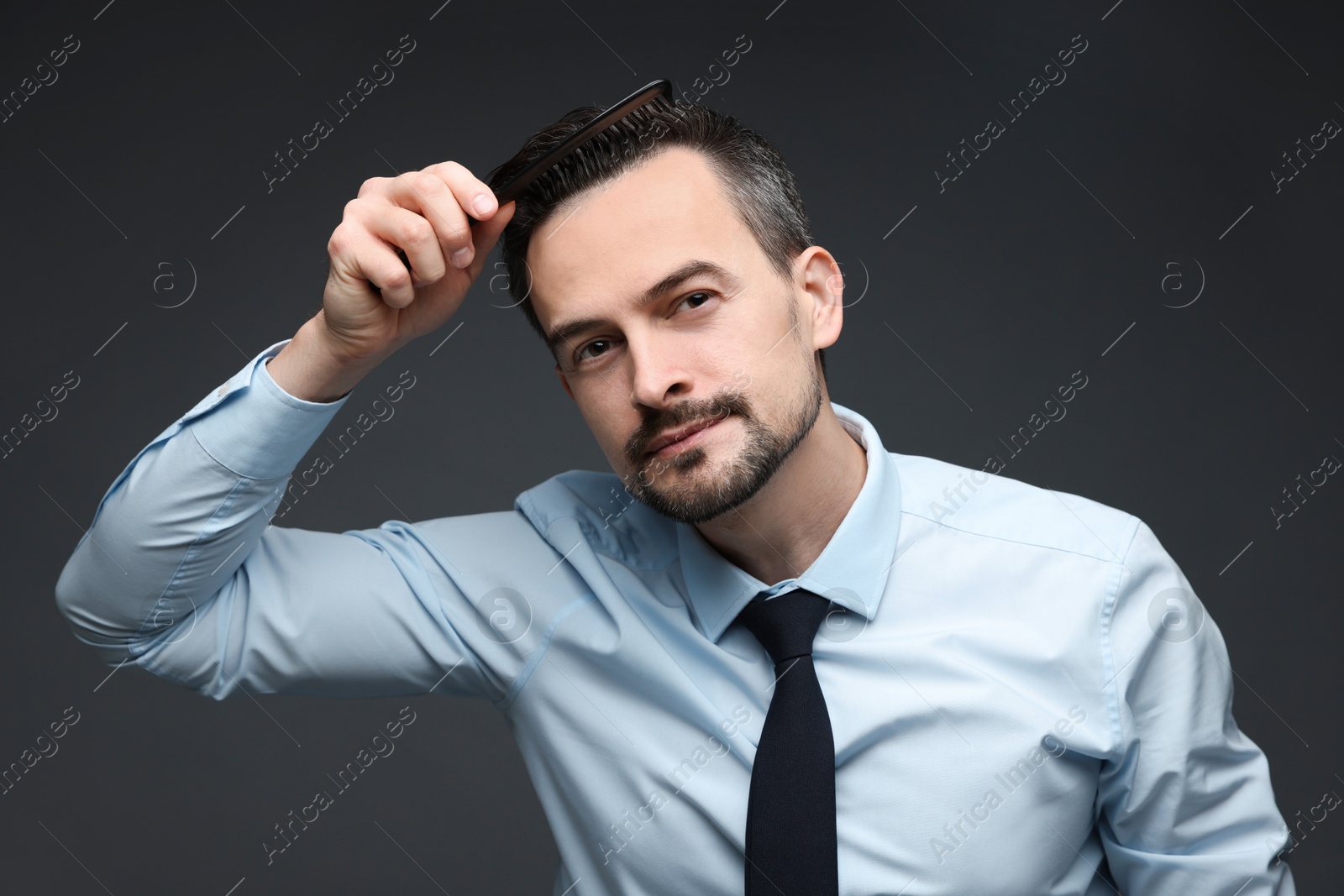 Photo of Handsome man combing his hair on dark background