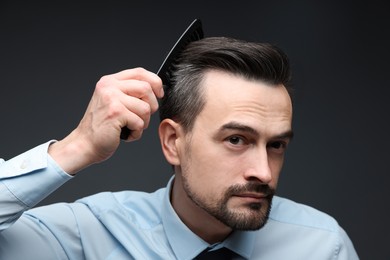 Photo of Handsome man combing his hair on dark background